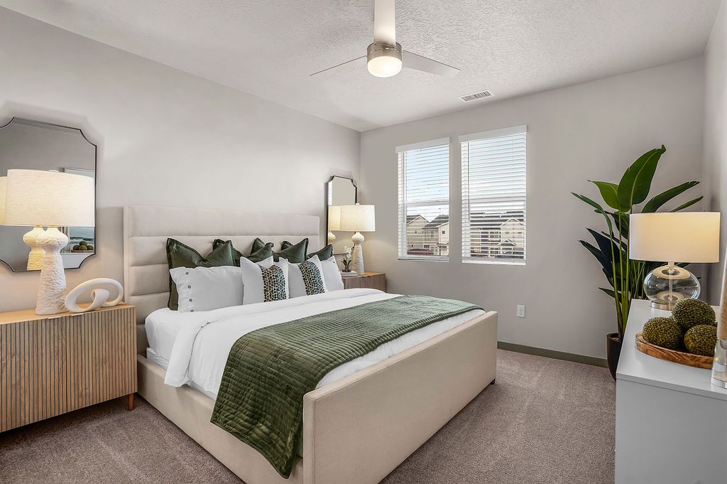 Bedroom in a modern apartment with a plush bed, two windows, and neutral decor.