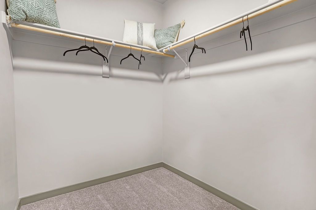 Walk-in closet with two hanging rods, a shelf above, and decorative pillows.