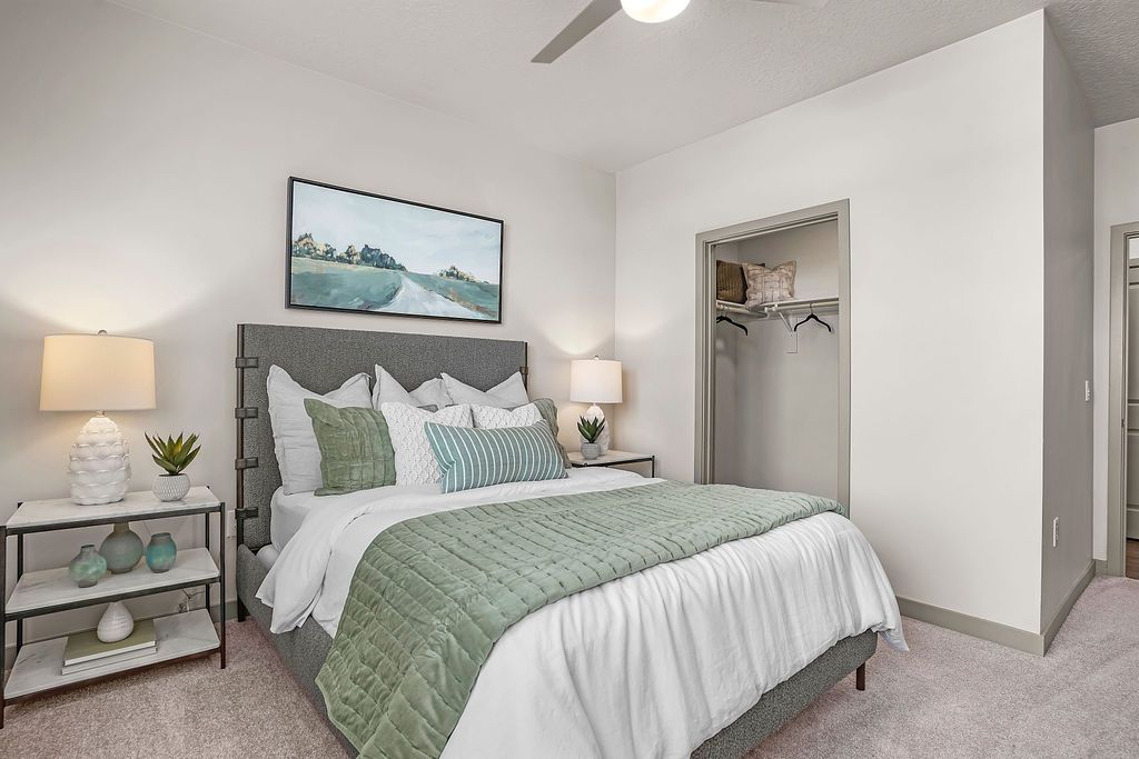 Bedroom in an apartment featuring a queen bed with gray upholstered headboard, two nightstands, and an open closet.