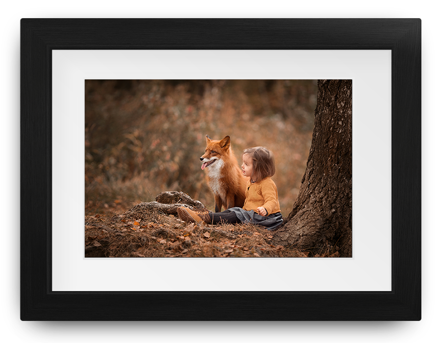 Framed photo of a child with a fox in a forest, both sitting among autumn leaves.