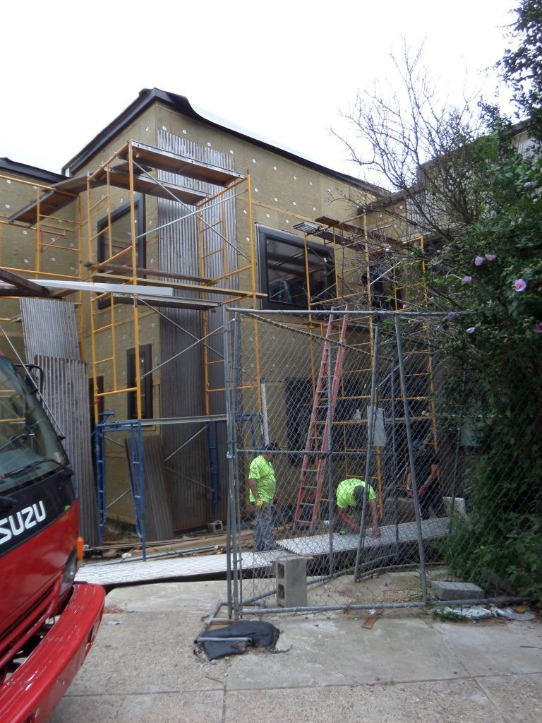 Building under construction; scaffolding, workers, red truck, and a chain link fence.
