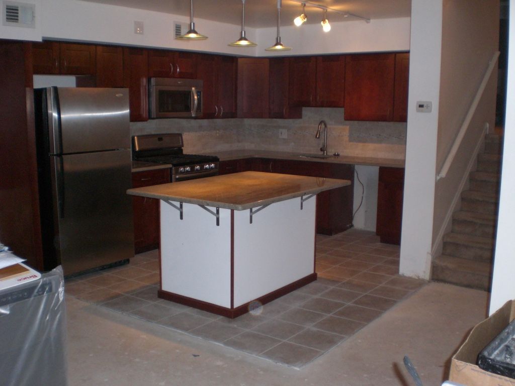 Kitchen with dark wood cabinets, stainless steel appliances, and island with a light-colored countertop.
