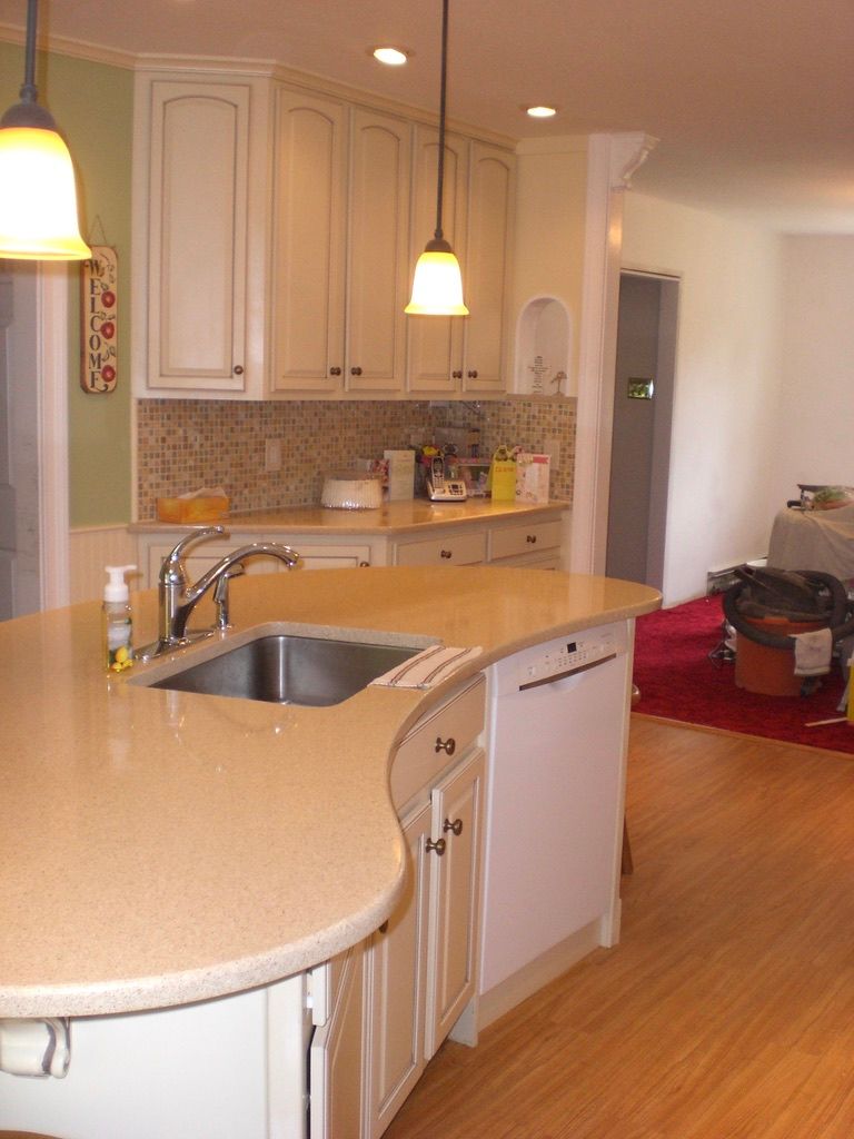 Kitchen with white cabinets, light countertops, and an island with a sink and dishwasher.