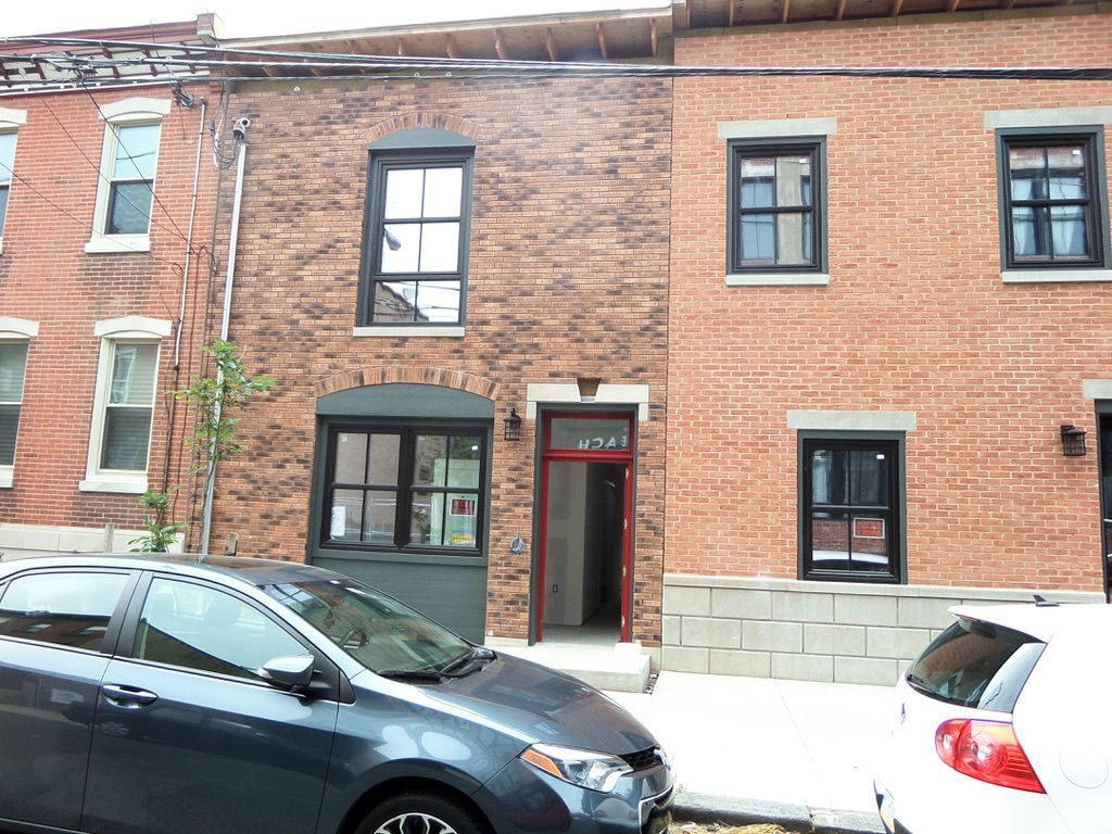 Row of brick buildings with cars parked in front.