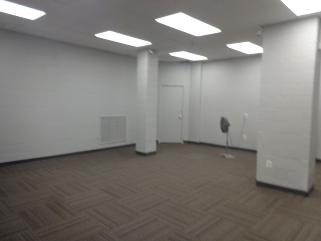 Empty office with white walls, carpet flooring, and overhead lights.