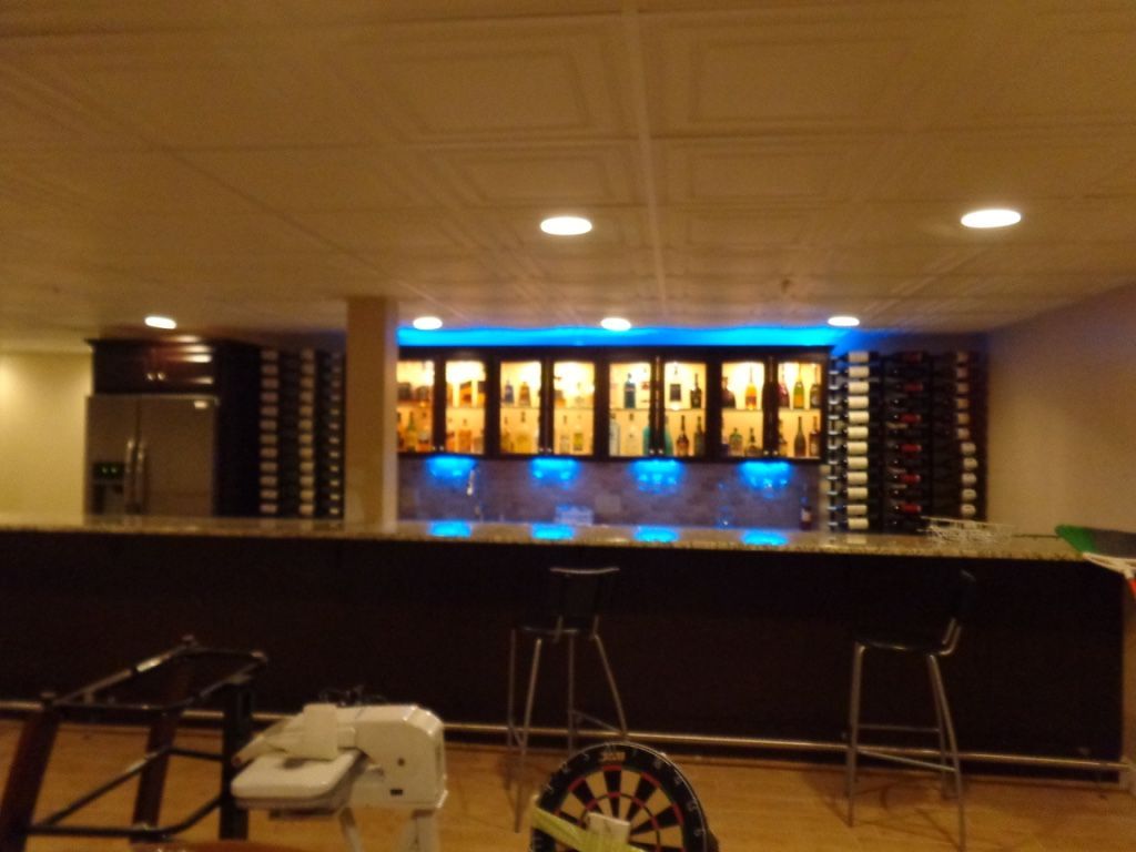Basement bar with liquor display and seating. Dark wood and marble countertops, blue lights.