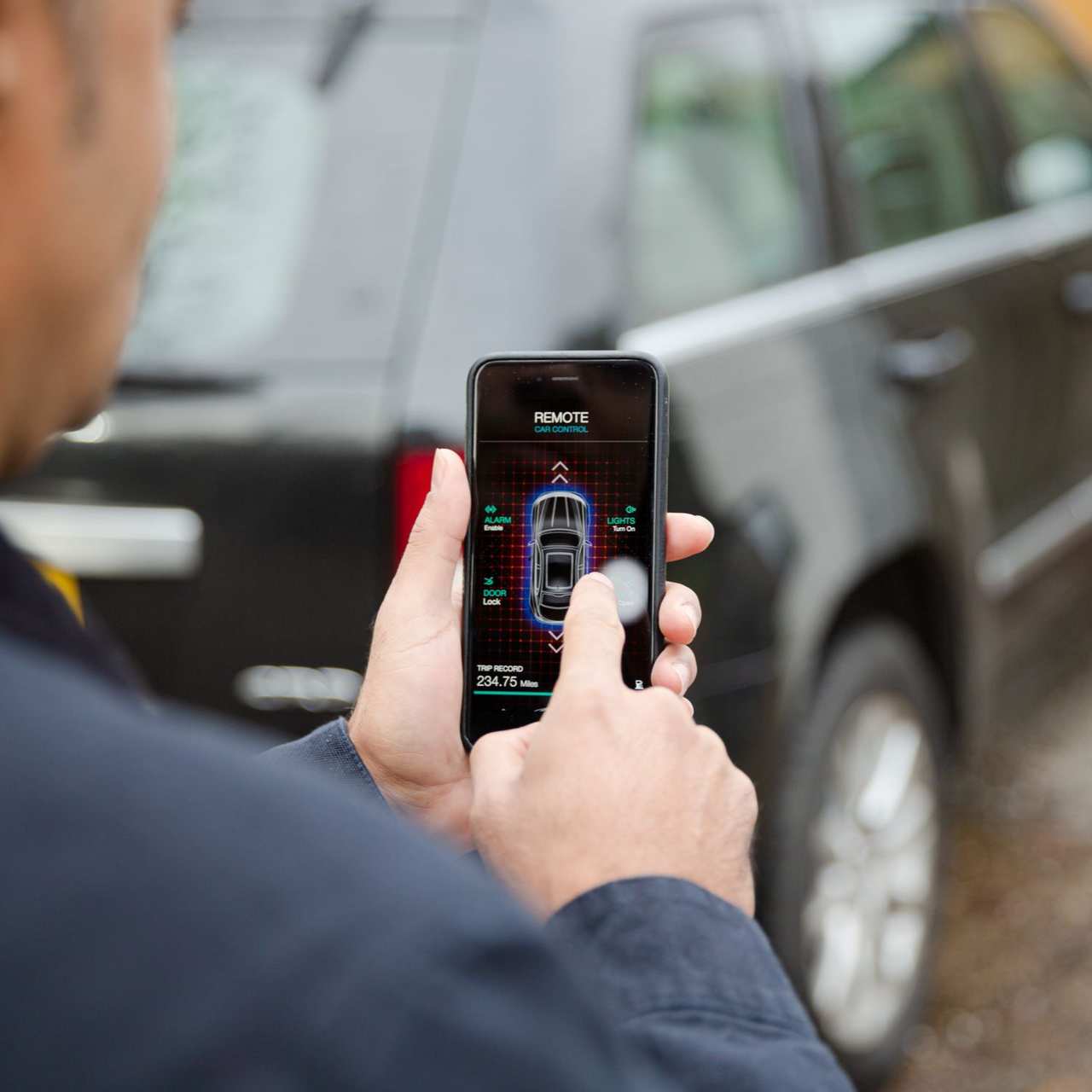 Person using a smartphone to remotely control a vehicle, likely parking it, with graphic representation of the car's surroundings on the screen.