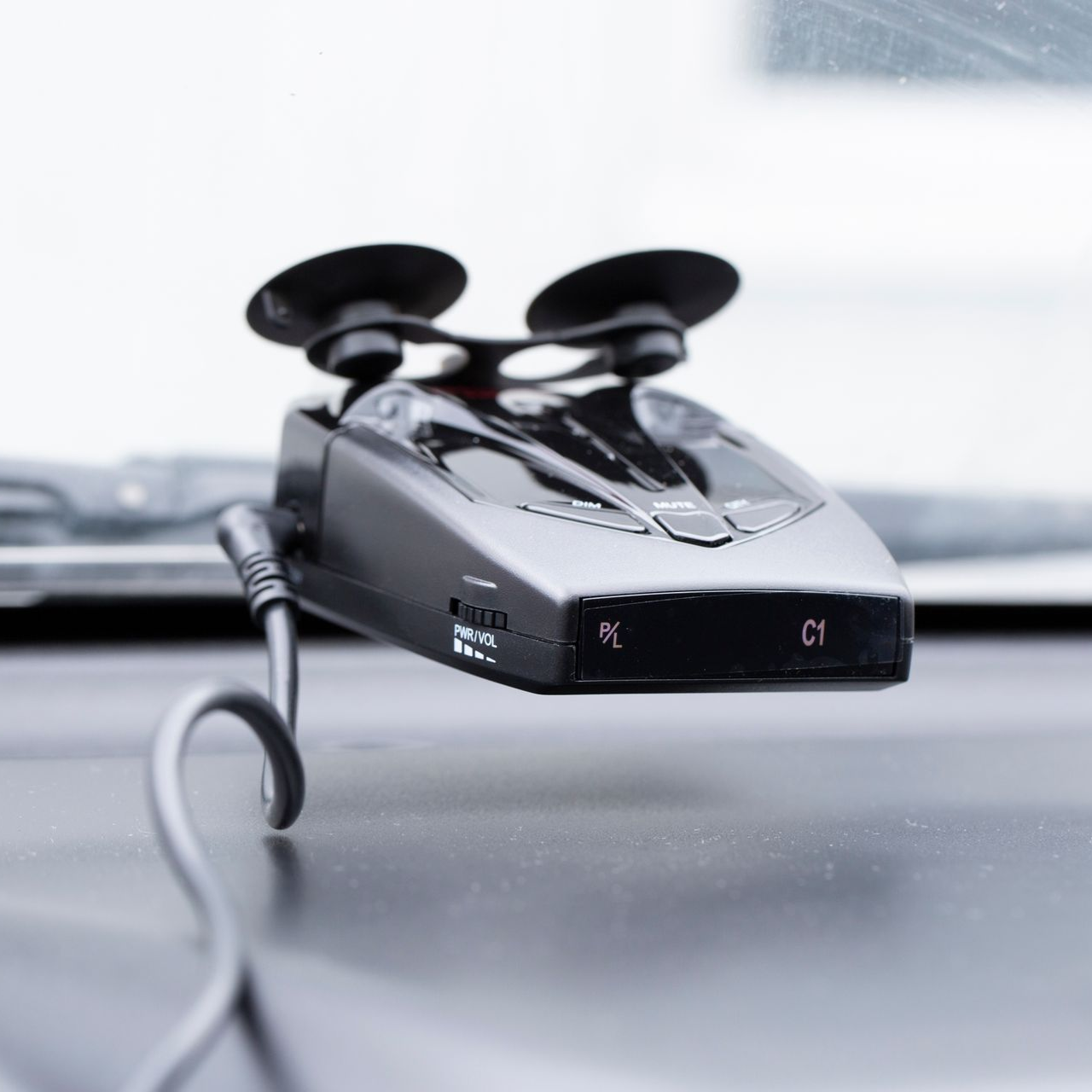 Black radar detector mounted on a car dashboard with a suction cup, showing illuminated 
