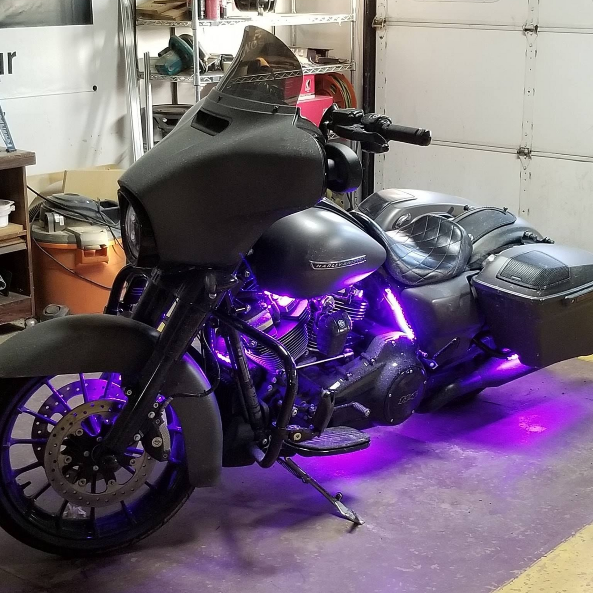 Black Harley-Davidson motorcycle with purple underglow, in a garage.