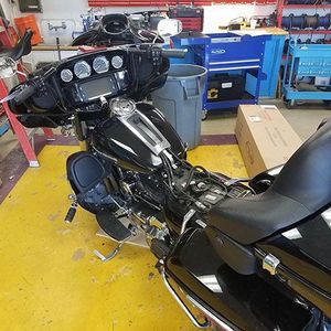 Black motorcycle in a repair shop with tools and a toolbox in the background.