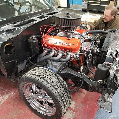 Black car engine bay with a large orange V8 Chevy engine, man working.