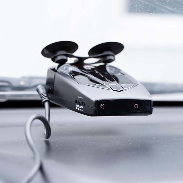 Black radar detector mounted on a car dashboard with a suction cup, showing illuminated 