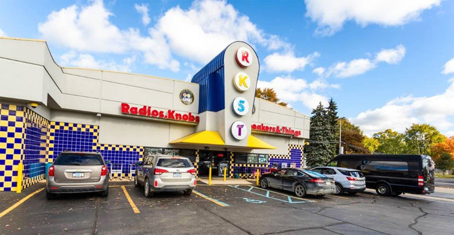 Exterior of "Radio Knob" building with a few cars parked in front.
