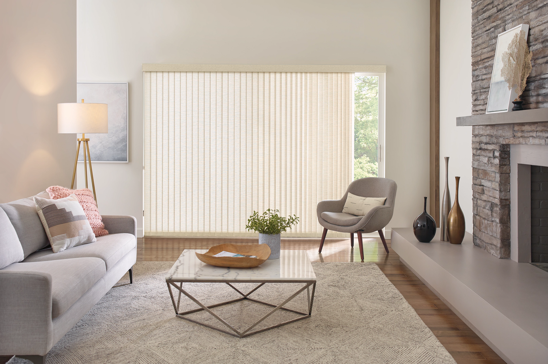 Modern living room with gray sofa, wicker chair, coffee table, large window blinds, and stone fireplace