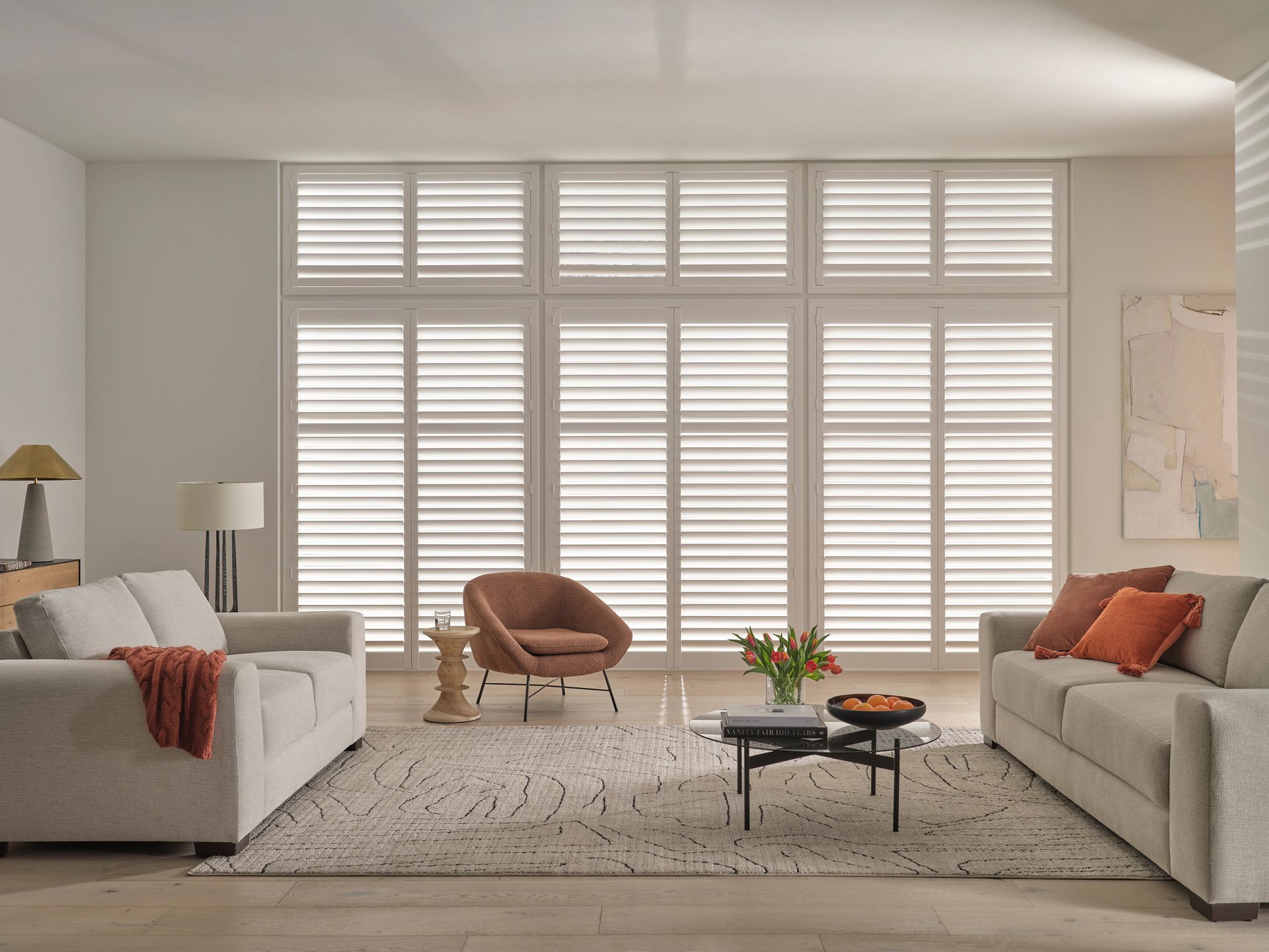 Bright modern living room with two beige sofas, a pink chair, and large shuttered windows