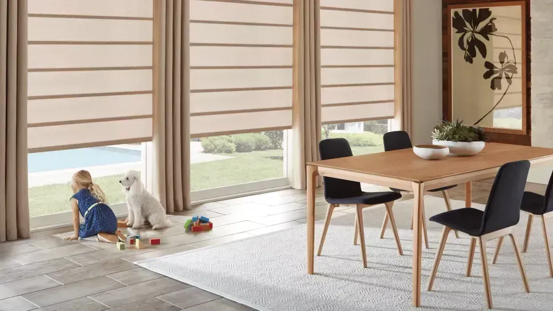 Bright dining room with wooden table and black chairs; a child plays on the floor by large windows.
