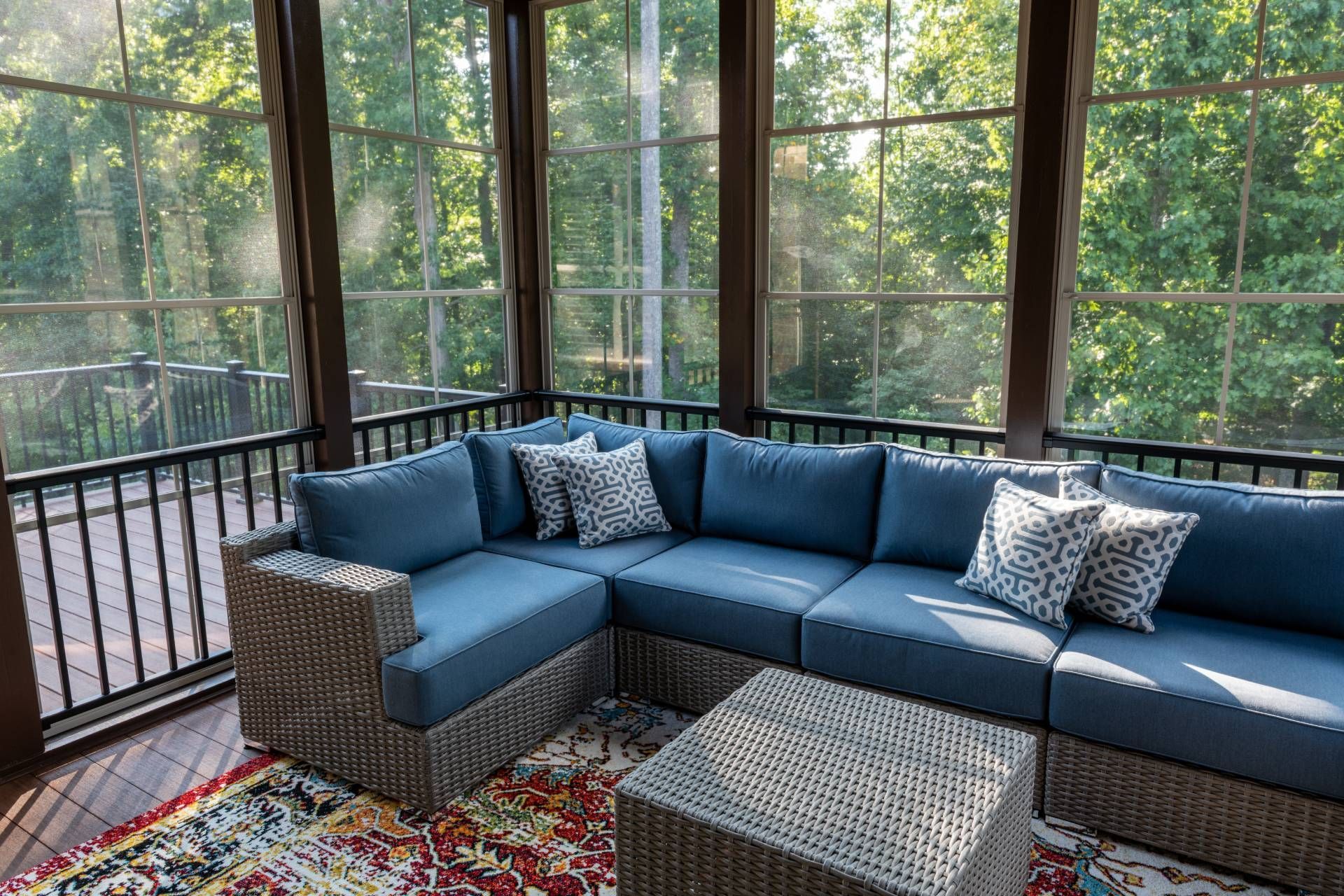 A sunroom, surrounded by lush green trees, with expansive windows in need of proper window treatment