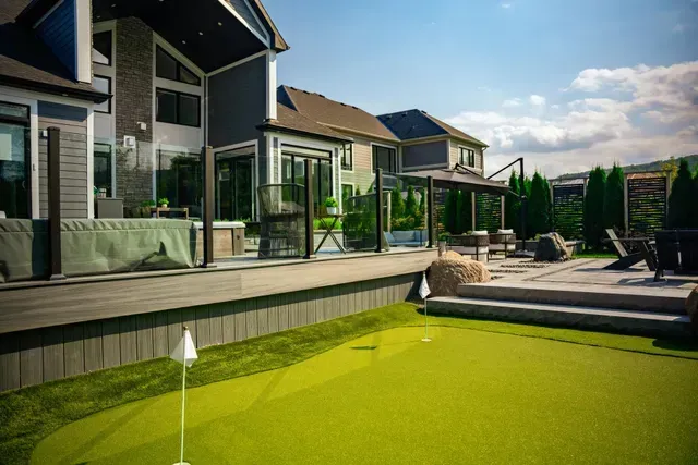There is a putting green in the backyard of a house.