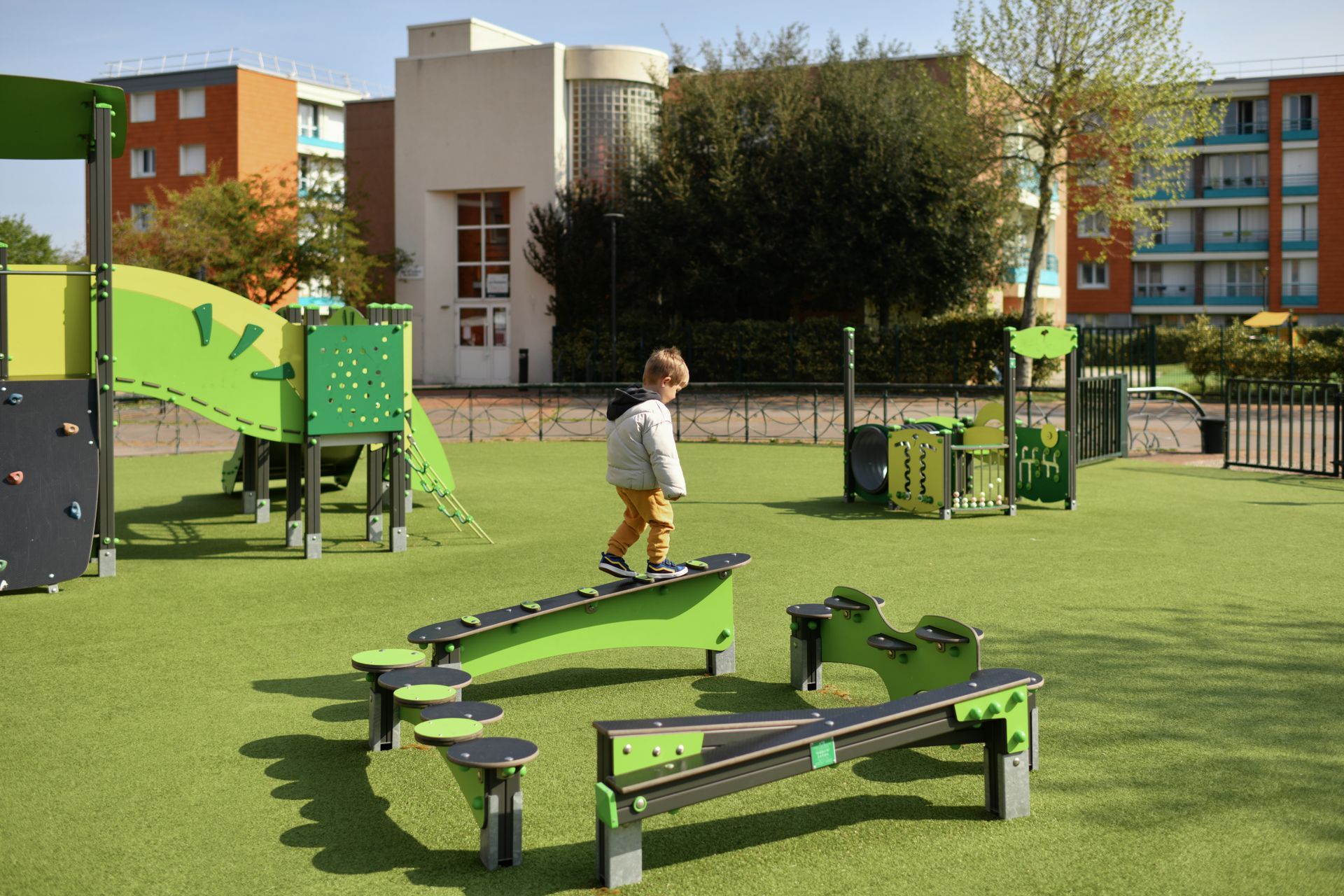 A little boy is standing on a bench in a playground.