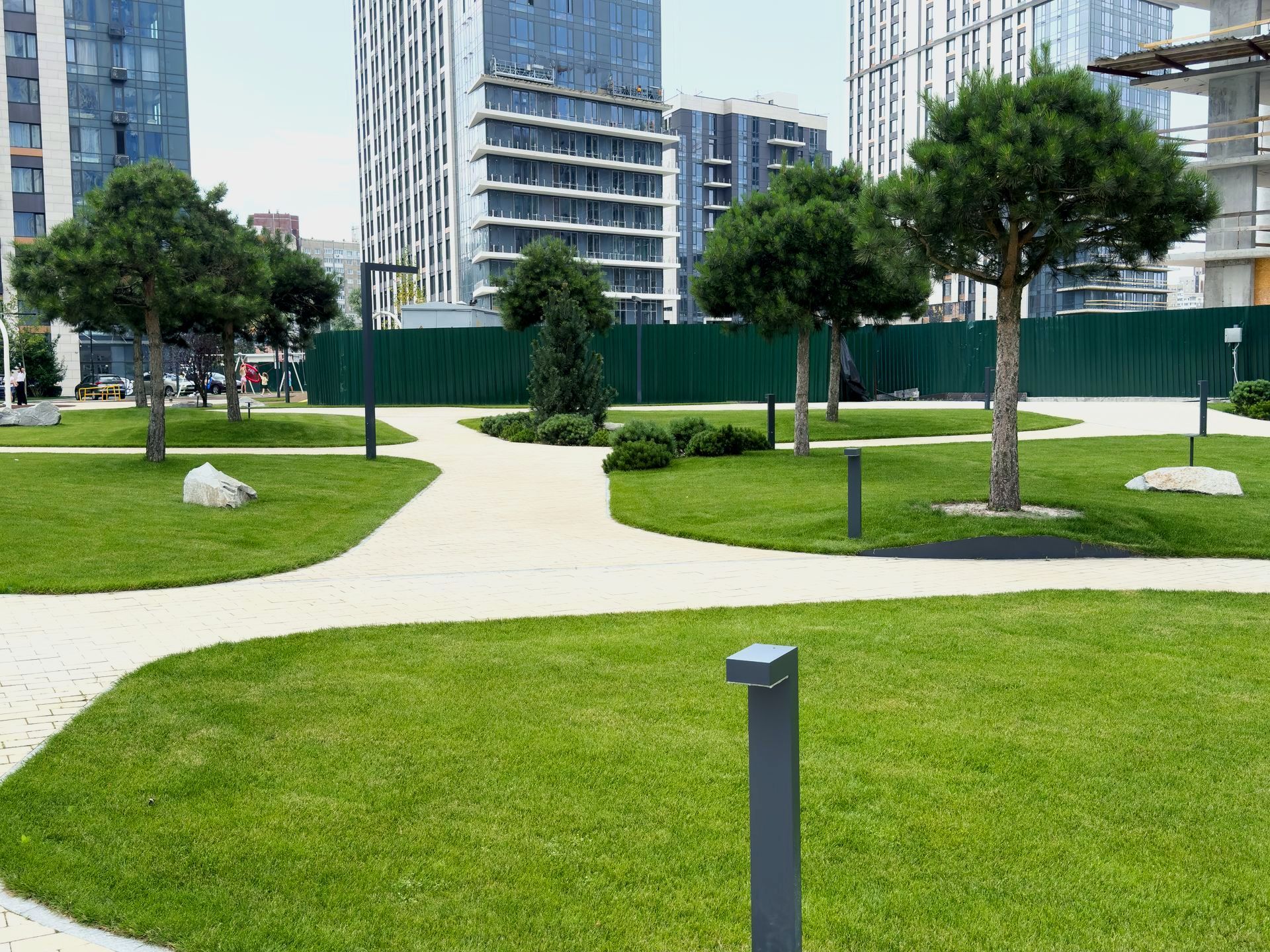 A park with a lot of grass and trees in front of a building.