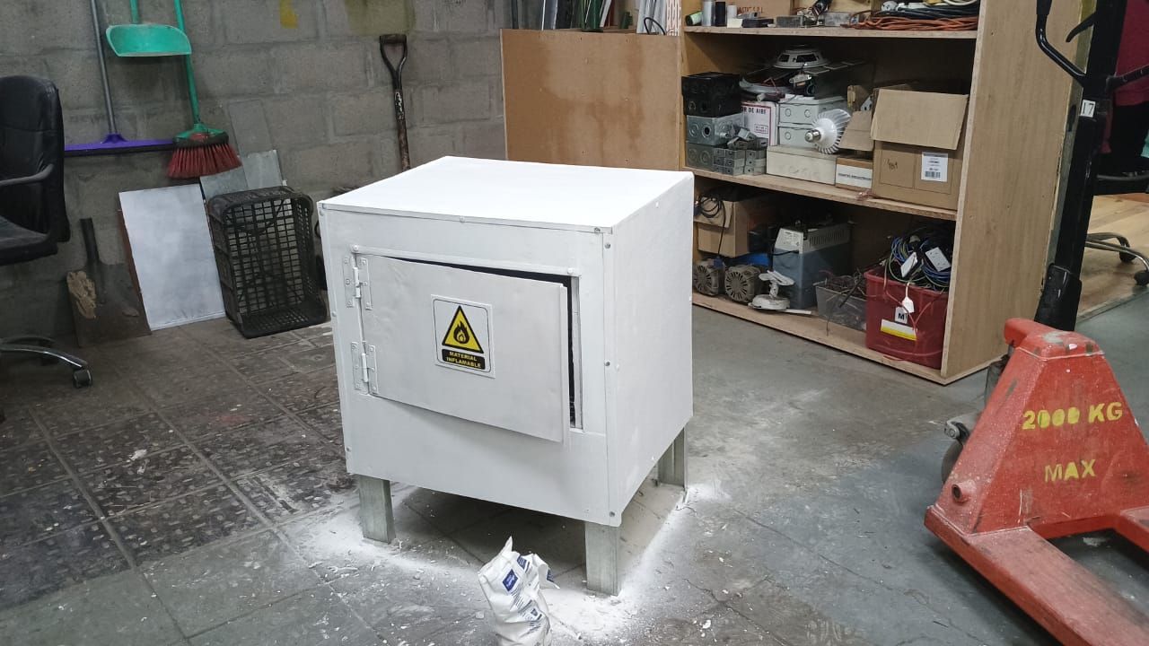 Caja eléctrica blanca con símbolo de advertencia, en un entorno de taller, sobre un piso de concreto.