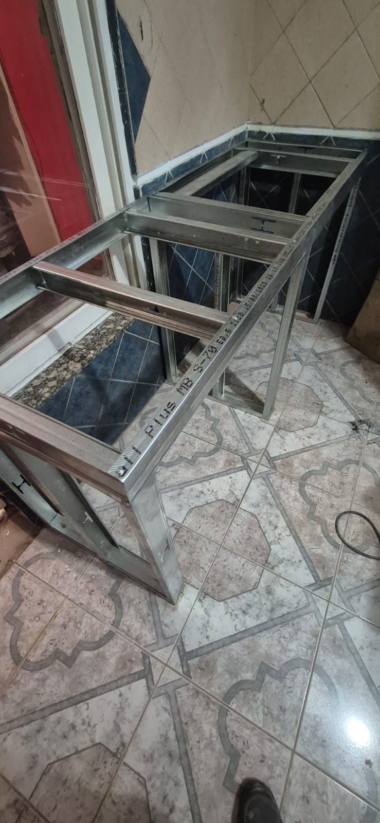 Construcción con estructura de metal sobre piso de baldosas estampadas, posiblemente para mostrador o gabinete.