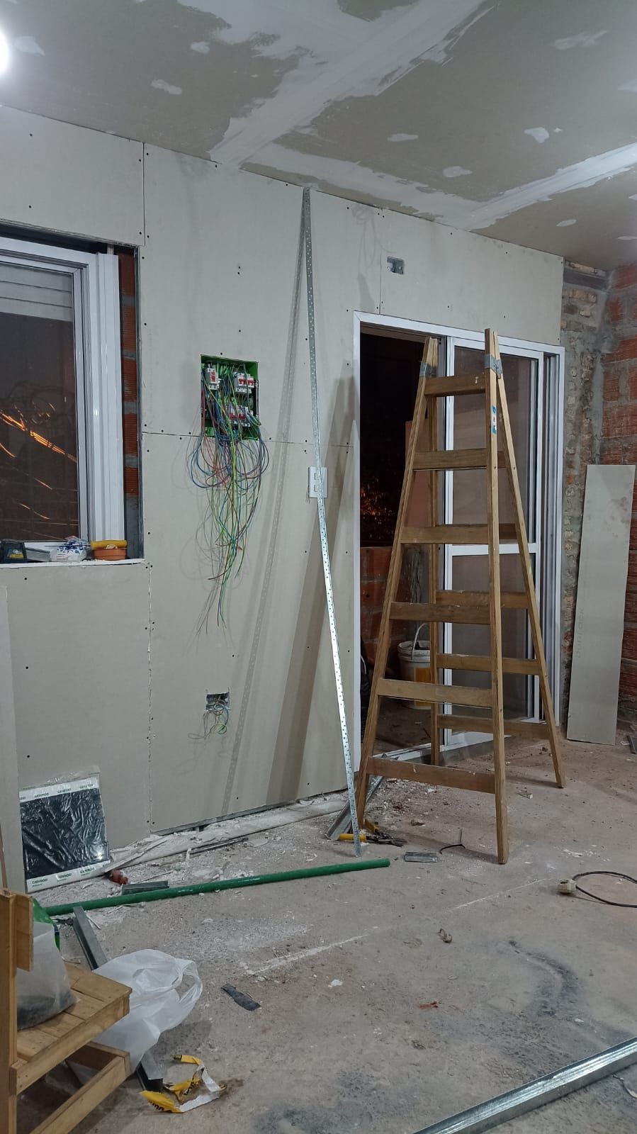 Un hombre con camisa azul usa un destornillador para arreglar la cerradura de una puerta. Una llave cuelga del pomo.