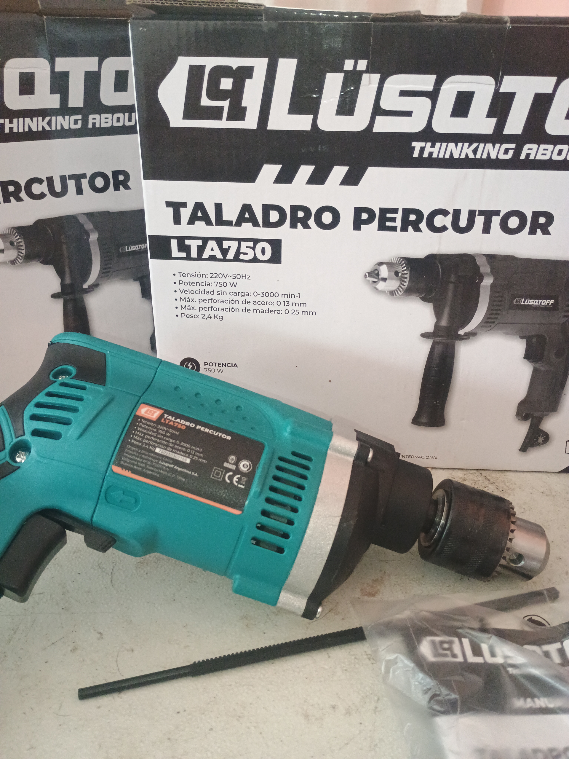 Taladro percutor LSQT LTA750 color verde azulado y negro delante de su caja.