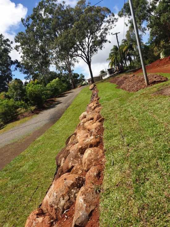 Stone Retaining Wall Next to a Sloping Lawn and Road Under a Cloudy Sky — Macca's Dynamic Earthworks in Tolga, QLD