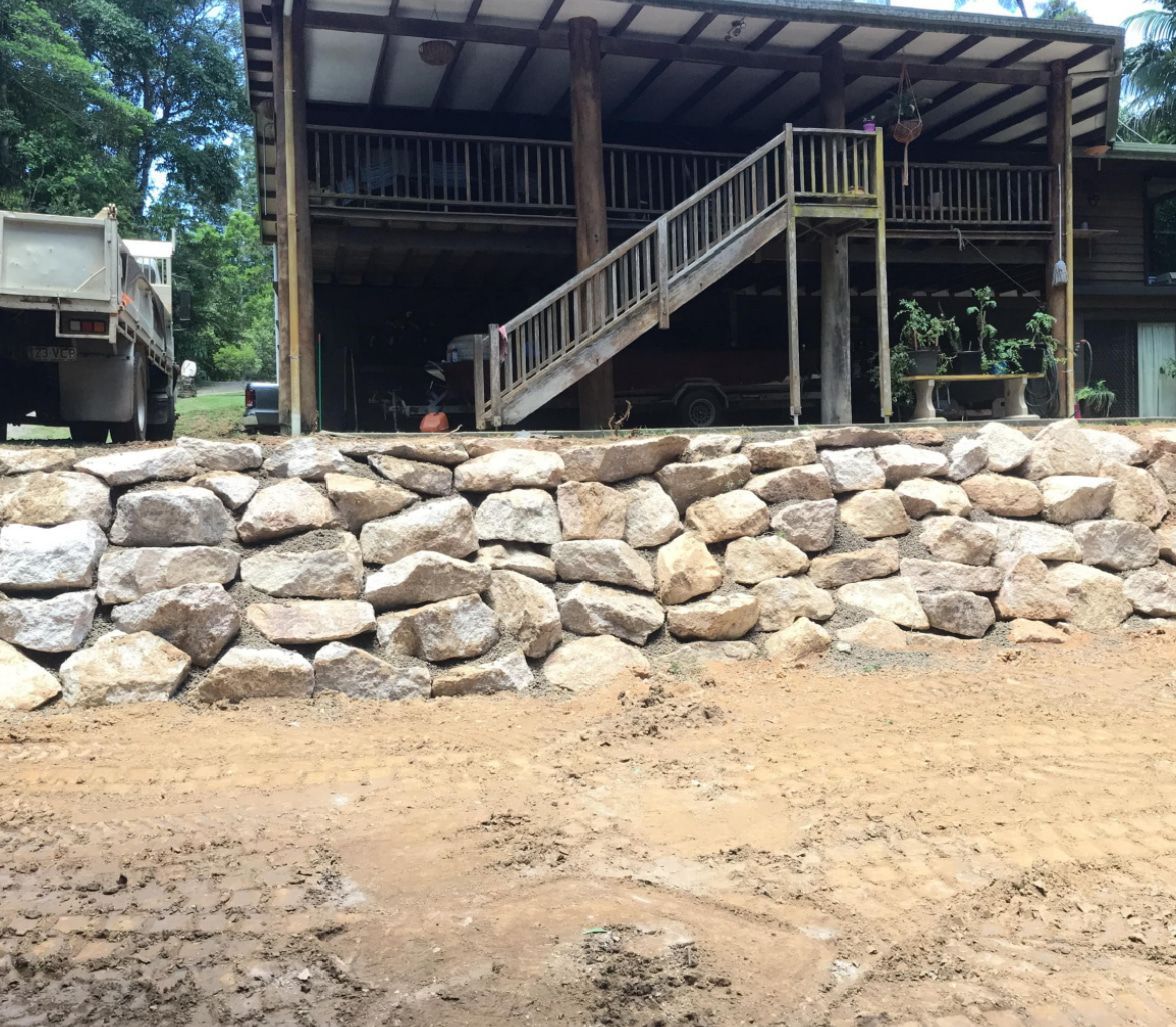 Rock Retaining Wall in Front of A House with Stairs and A Truck in The Background — Macca's Dynamic Earthworks in Tolga, QLD