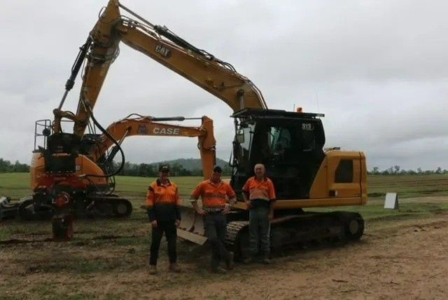 Three Construction Workers Stand in Front of A Excavator — Macca's Dynamic Earthworks in Tolga, QLD