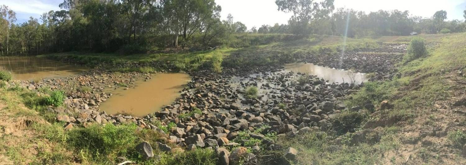 A Rock Filled Waterway with Muddy Water and Green Vegetation — Macca's Dynamic Earthworks in Tolga, QLD