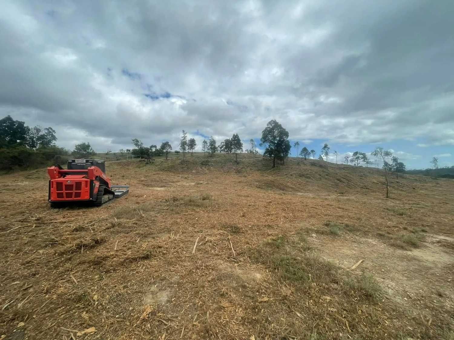 Orange Skid Steer Clearing a Field of Wood Chips — Macca's Dynamic Earthworks in Ravenshoe, QLD