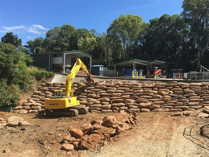 Yellow Excavator Placing Stones on A Retaining Wall in A Construction Site — Macca's Dynamic Earthworks in Tolga, QLD