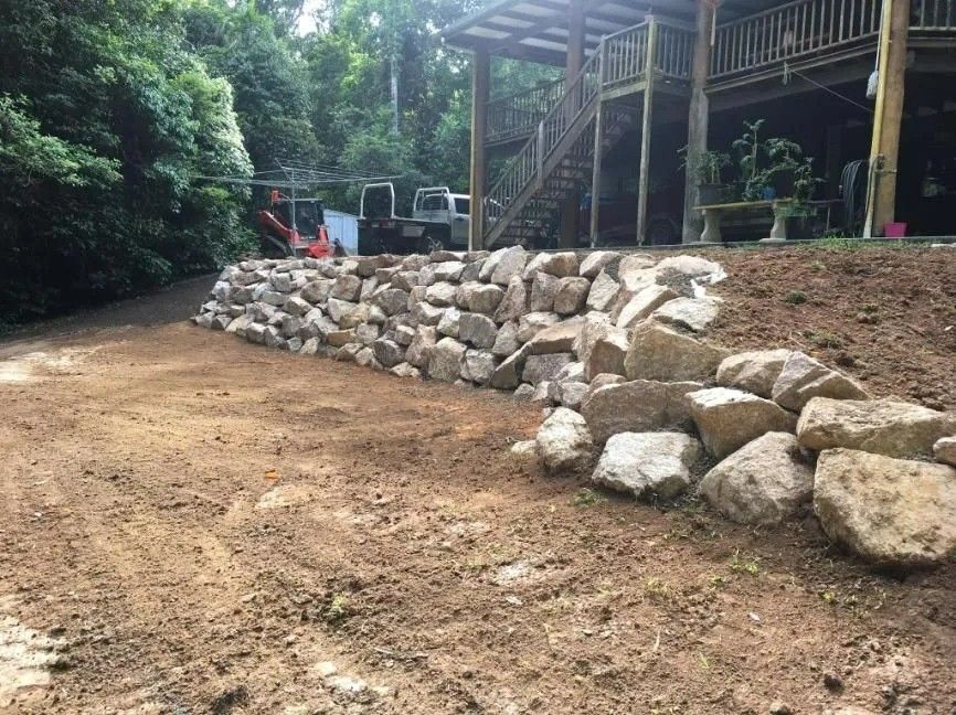 A Stone Retaining Wall Next to A Dirt Driveway — Macca's Dynamic Earthworks in Ravenshoe, QLD
