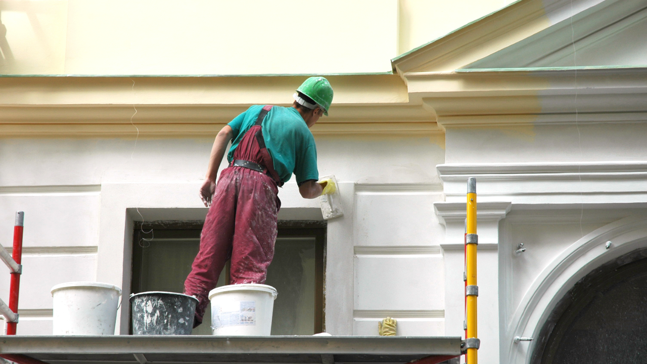 A man is standing on a scaffolding painting a building.