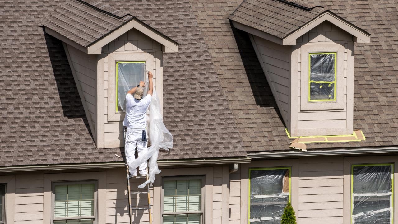 A man is standing on a ladder painting a house.