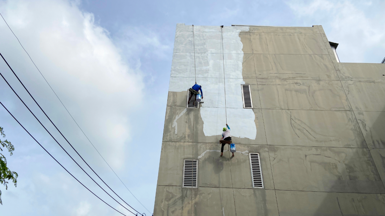 Two people are painting the side of a building.