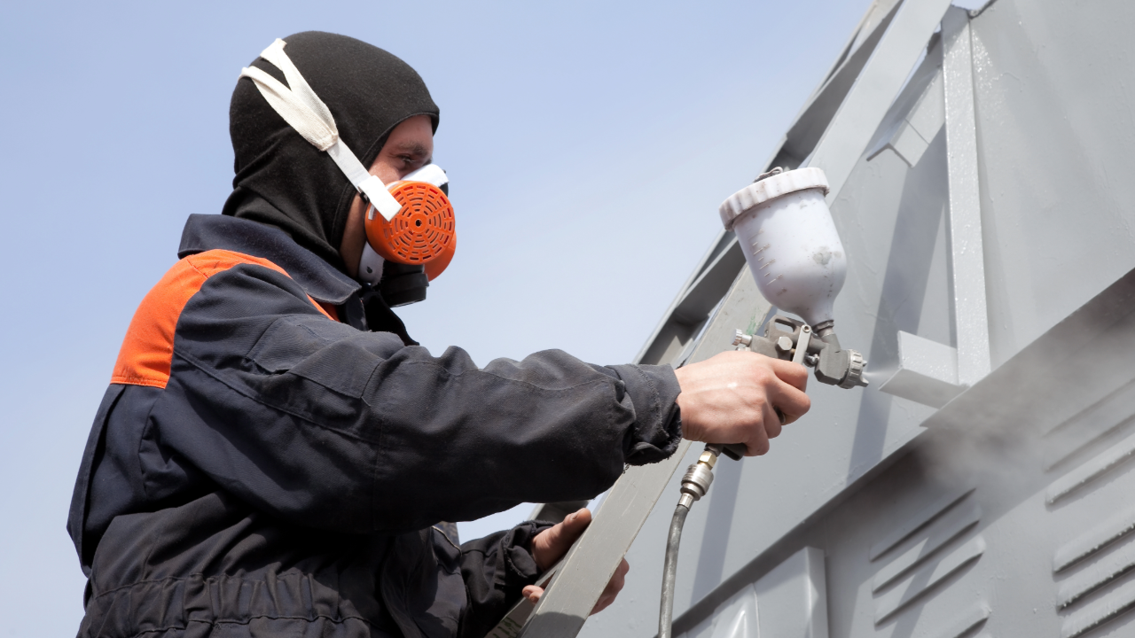 A man wearing a mask is spray painting a building