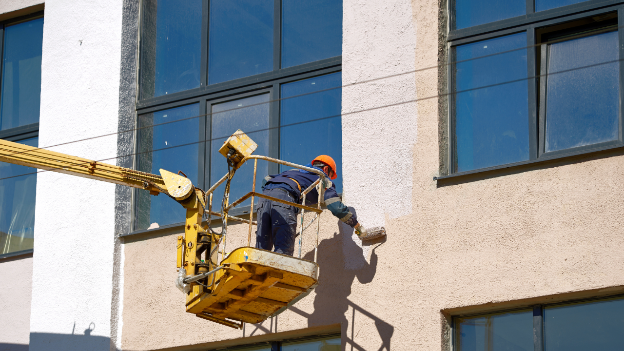 A man is cleaning the windows of a building with a crane.