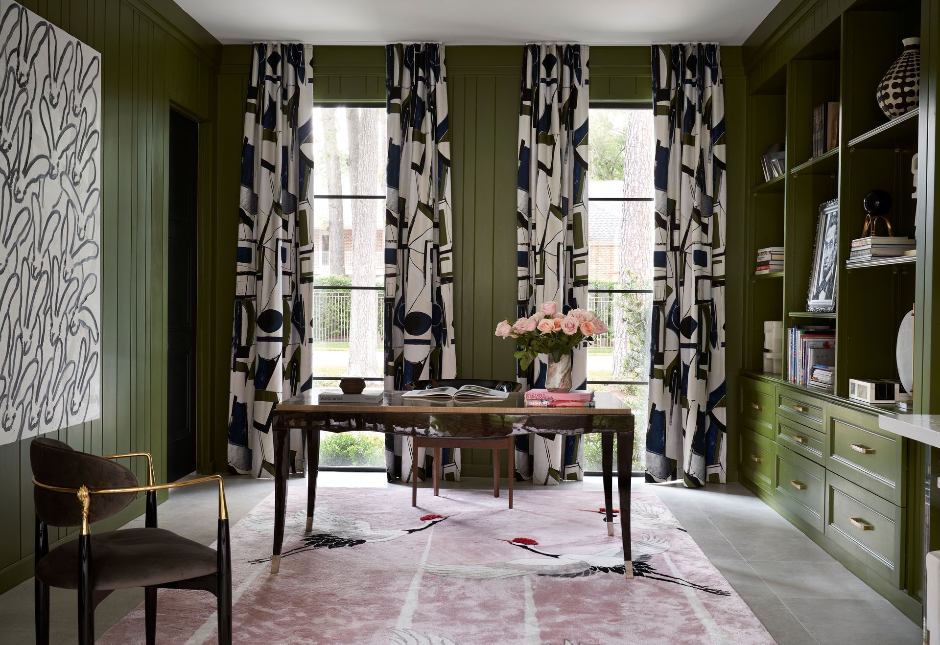 a home office with green walls , a desk , chair , rug and curtains .