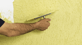 una mano che spatola un muro con della vernice gialla