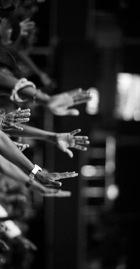 A black and white photo of a crowd of people raising their hands in the air.