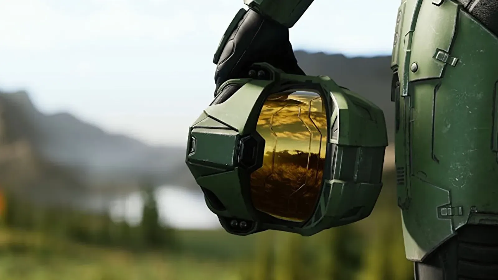 Green armored figure holding a Master Chief helmet, reflecting a grassy field and sky.