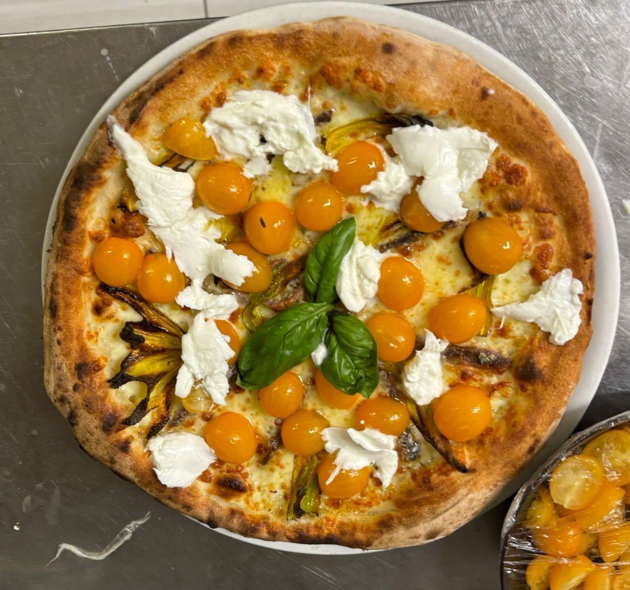 Pizza condita con pomodori gialli, formaggio bianco e basilico su un piatto bianco.