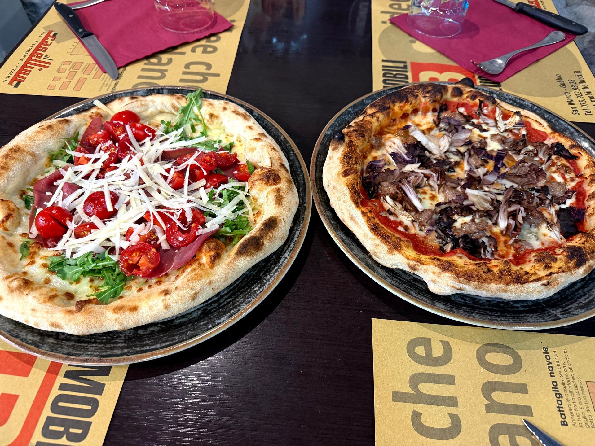 Due pizze su piatti, una con pomodoro e formaggio, l'altra con carne e funghi, su un tavolo di un ristorante.