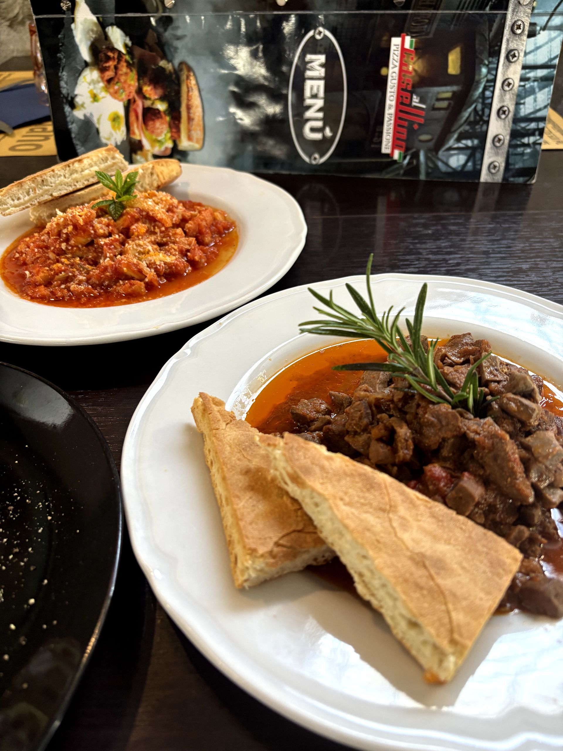 Due piatti di cibo su un tavolo: uno con salsa rossa e pane, l'altro con carne, rosmarino e pane.