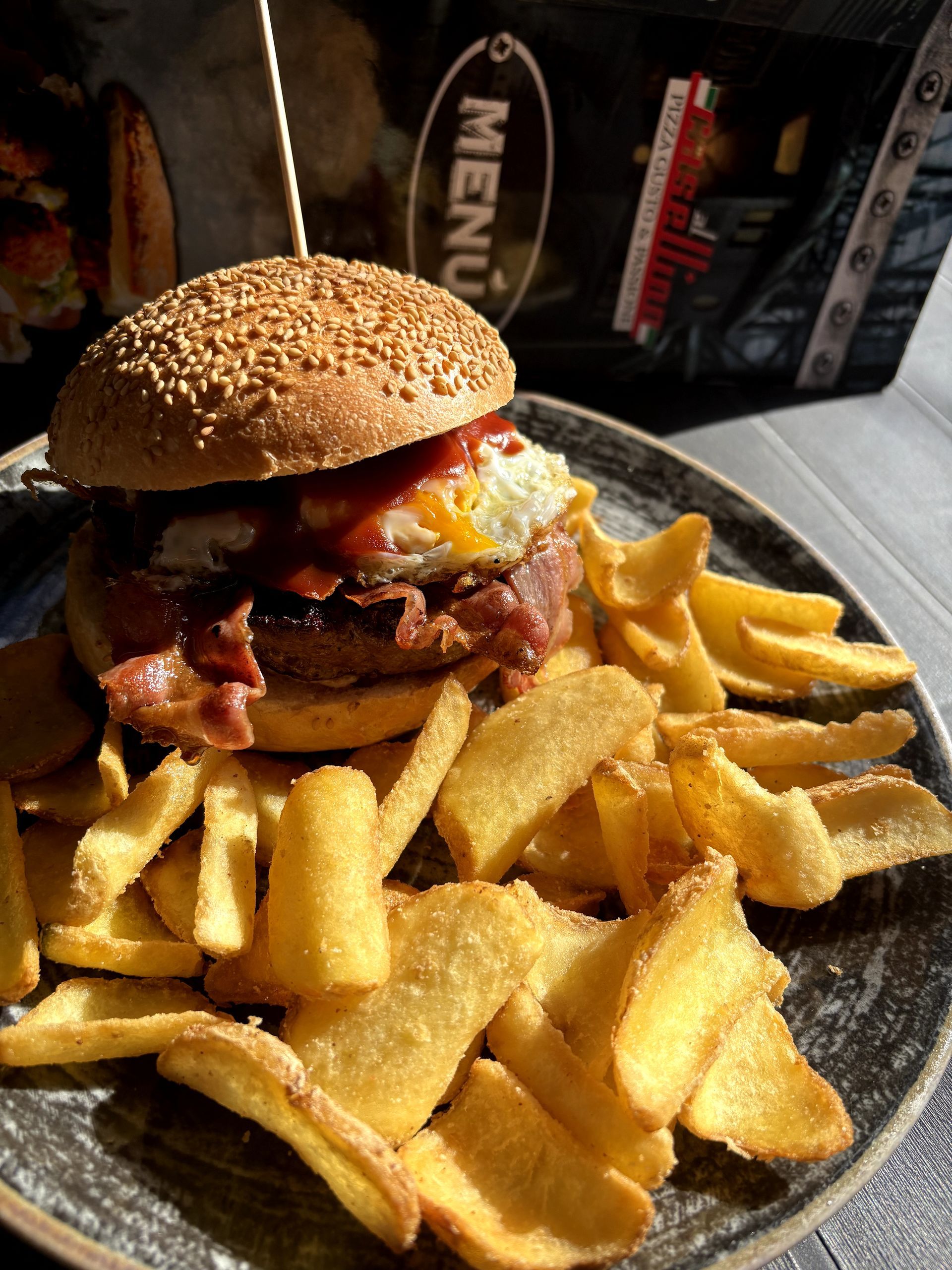 Hamburger con pancetta, uova e patatine fritte su un piatto accanto al menu.