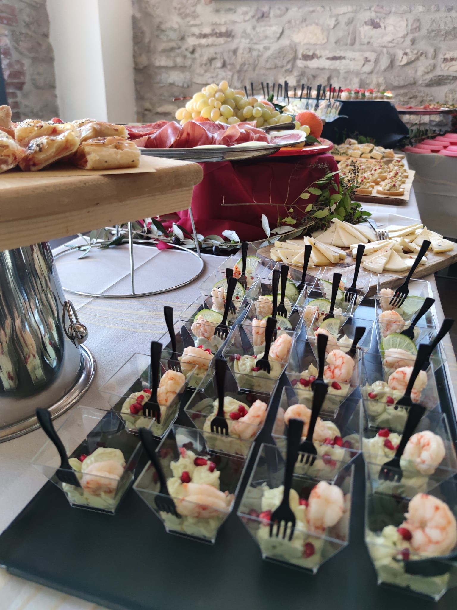 Tavolo a buffet con antipasti e pietanze: gamberi, pasticcini, frutta e salumi.