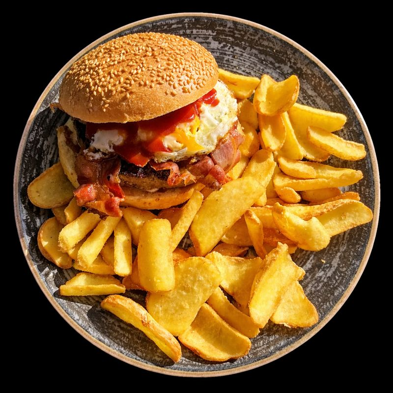 Hamburger con uova e pancetta, patatine fritte su un piatto.